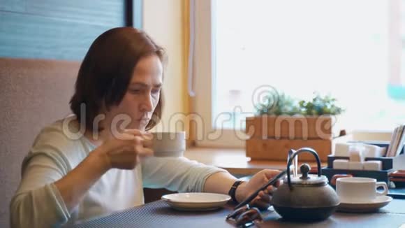 女人在咖啡馆喝茶手里拿着智能手机一位女士查看她的智能手机上的电子邮件并在视频的预览图