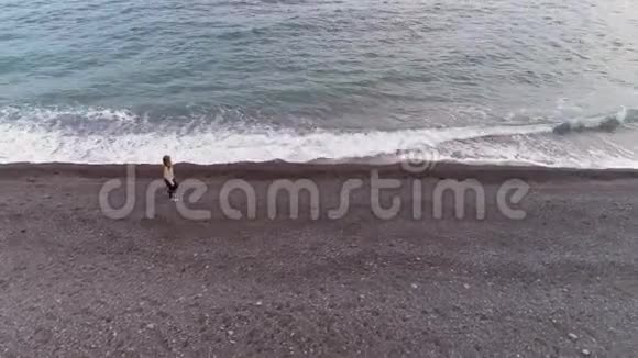 年轻的女人正带着飞溅的波浪走在海边鸟瞰图视频的预览图