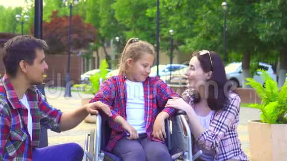 看镜头的画像爸爸妈妈带着一个残疾的小女儿坐在轮椅上开心视频的预览图