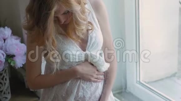 穿着白色连衣裙的孕妇正坐在窗边穿着白色蕾丝连衣裙从上面看幸福的女人期待着视频的预览图