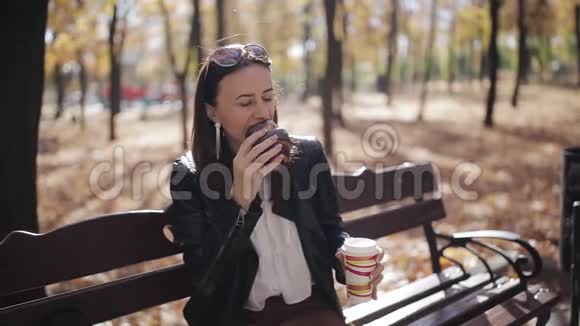 在公园长椅上吃羊角面包和喝纸杯咖啡的女商人视频的预览图