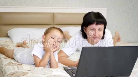 幸福家庭母婴躺在床上看手提电脑屏幕视频的预览图