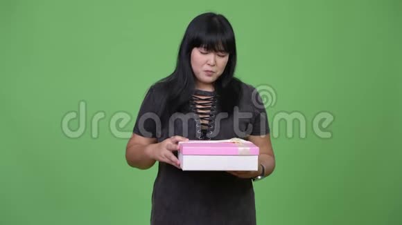 美丽的超重亚洲女人打开礼品盒看上去很惊讶视频的预览图