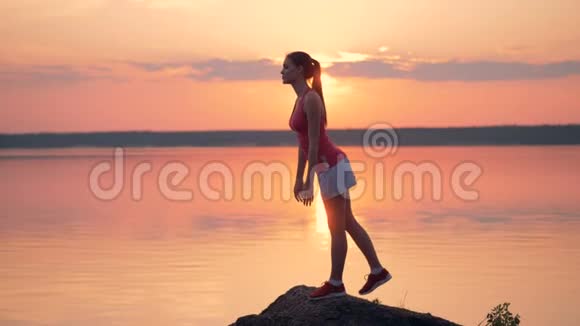 美丽的女士在日出时在湖边的山上做运动视频的预览图