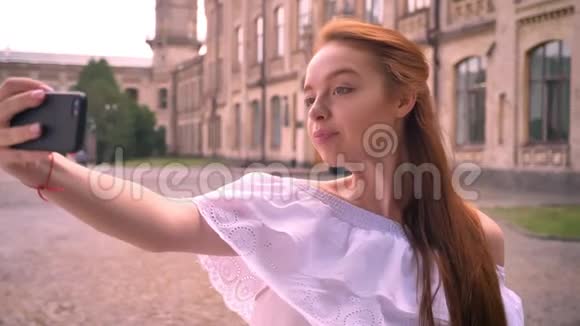 美丽的姜女光着肩膀用手机自拍微笑着站在街上视频的预览图