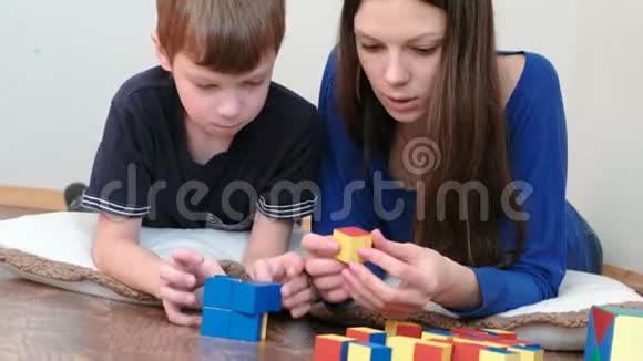 妈妈和儿子一起玩木制彩色教育玩具积木躺在地板上他们建造了一个蓝色的盒子视频的预览图