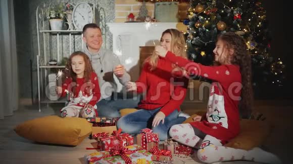 幸福的家庭有四个人他们带着火花微笑着看着圣诞树脚下的摄像机视频的预览图