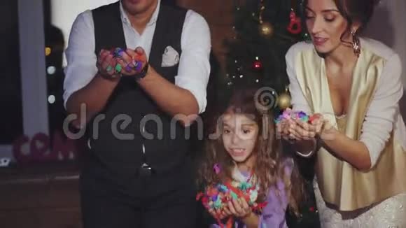 圣诞快乐爸爸妈妈和女儿吹着五颜六色的五彩纸屑庆祝活动视频的预览图