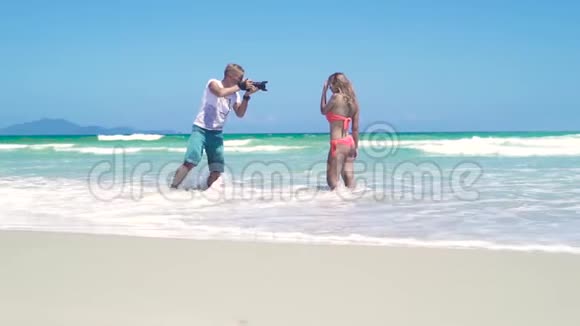 男摄影师拍摄年轻女子比基尼在海滩上摆姿势年轻的摄影师视频的预览图