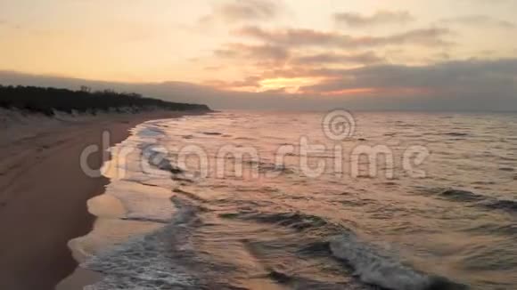 空中观看无人机镜头低飞行在一个废弃的海滩上日落带着滚滚海浪和夕阳的沙岸视频的预览图