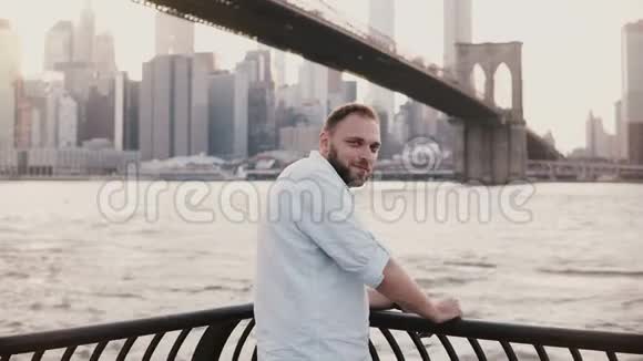 成功的白种人自由商人在布鲁克林大桥路堤4K附近的相机微笑的中镜头肖像视频的预览图