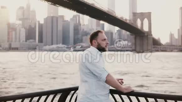 快乐的欧洲商人站在纽约布鲁克林大桥的河堤围栏旁看着智能手表4K视频的预览图