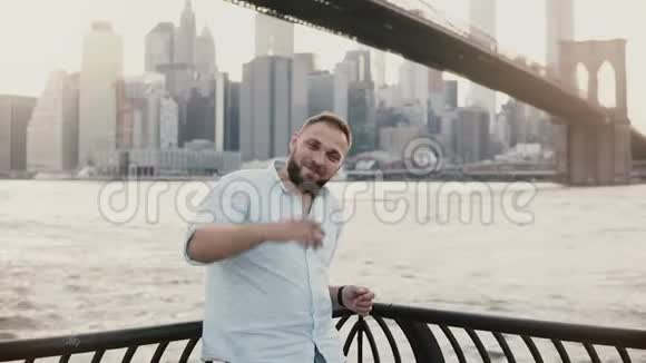 快乐成功的白人男子微笑着看着镜头展示手势指着4K背后令人惊叹的纽约城市风光视频的预览图