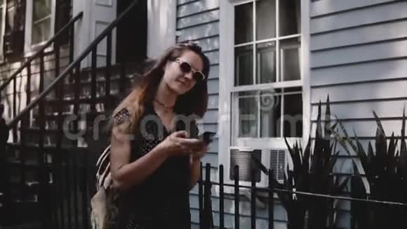 快乐快乐的高加索女人沿着纽约的街道走着美丽的房子使用智能手机应用程序慢动作视频的预览图