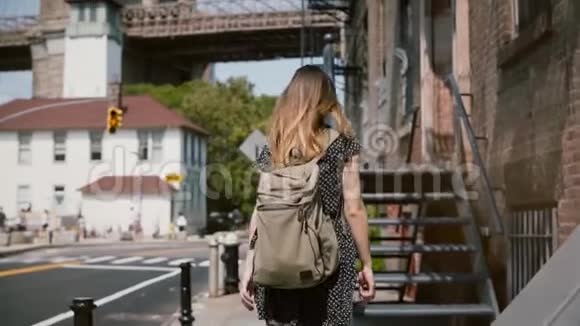 年轻女子背着背包和长发走上旧金属楼梯进入红砖建筑慢速行走视频的预览图