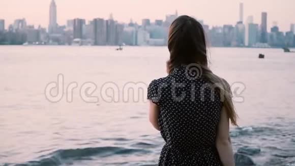 体贴的年轻白种人女孩头发在风中吹着看着日落在纽约市的河岸慢动作视频的预览图