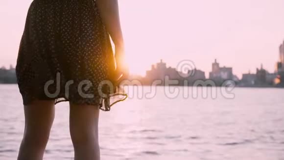穿着黑色礼服的女腿在风中摇曳站在美丽清澈的夏日城市景观日落的慢动作视频的预览图