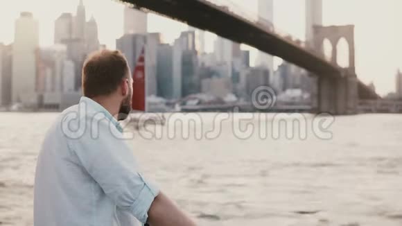 成功的白人自由商人站在纽约布鲁克林大桥下的河堤旁红船经过视频的预览图