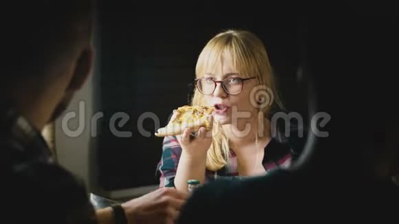年轻漂亮的戴眼镜的欧洲女孩喜欢吃比萨饼在一个休闲的家庭聚会上和朋友交谈视频的预览图