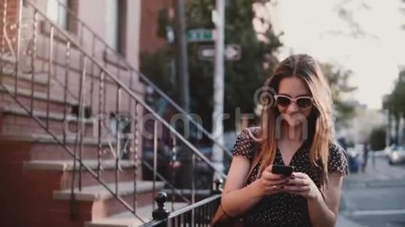 快乐的欧洲女孩长发微笑沿着古老的大红砖建筑散步使用智能手机应用程序慢动作视频的预览图