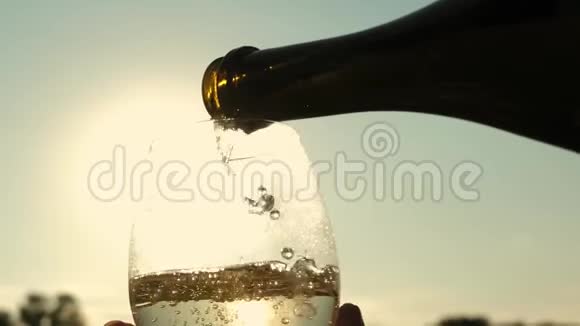 在日落的时候从瓶子里倒入起泡葡萄酒到透明的酒杯里恩爱夫妻的团队合作庆祝活动视频的预览图