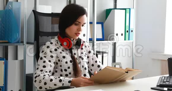 戴着红色耳机的女人在现代办公室看书视频的预览图