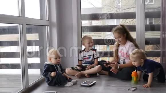 现代童年概念4个孩子坐在一起房间的地板上放着手机和平板电脑窗户是全景视频的预览图