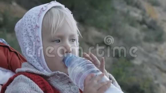 穿着帽衫和红色针织背心的小女孩在婴儿车里坐着塑料瓶喝牛奶或奶制品视频的预览图