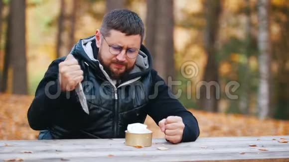一个男人坐在桌子旁用刀吃炖肉罐头视频的预览图