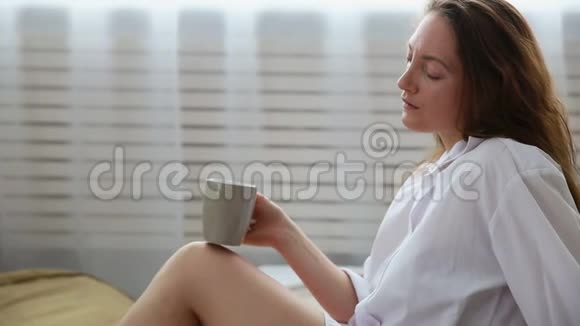 穿着白色衬衫女人在床上喝咖啡视频的预览图