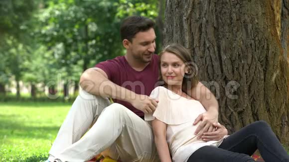 幸福的怀孕夫妇坐在公园里计划有保障的家庭生活福利视频的预览图