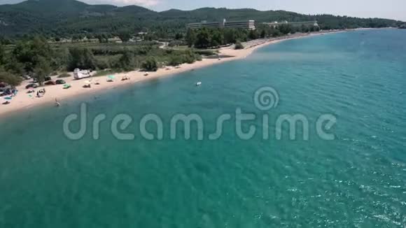 在希腊Halkidiki地区的一座小山下面的令人惊叹的蓝色海滩的空中景色用无人机前进和向下视频的预览图