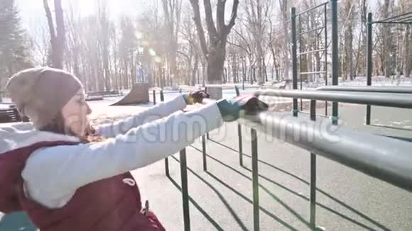 戴着手套穿着保暖背心的女运动员在户外运动场的高低杠上做运动的肖像视频的预览图
