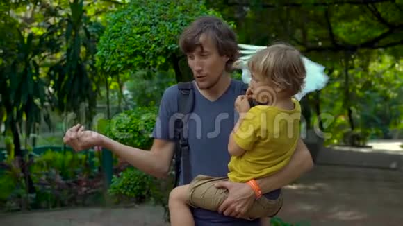 一个年轻人和他的小儿子在鸟公园玩得很开心用手喂白鹭视频的预览图