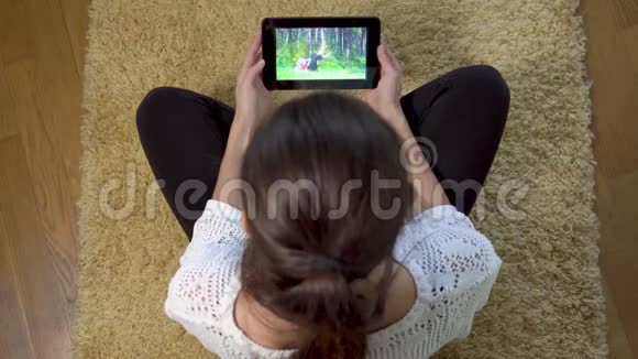 女孩使用平板电脑屏幕观看运动训练而坐在家里的地毯上视频的预览图