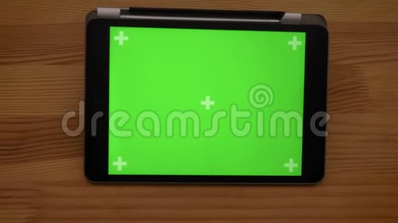 慢慢地拉开水平平板电脑的特写镜头在木制桌子背景上有绿色的屏幕视频的预览图