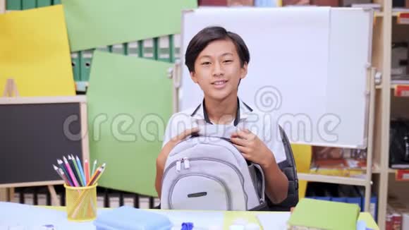 男孩抱着背包坐在桌子旁微笑着视频的预览图