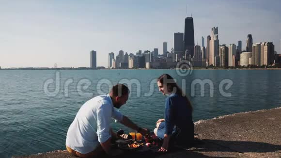 一对夫妇坐在密歇根湖畔吃早餐在芝加哥男人和女人在水边野餐视频的预览图