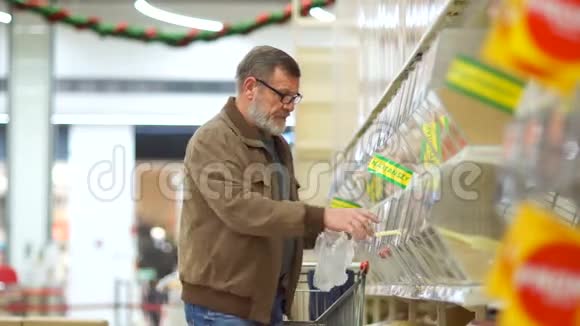 一位老人在超市的杂货店买谷物养老金领取者把车卷起来放到那里视频的预览图