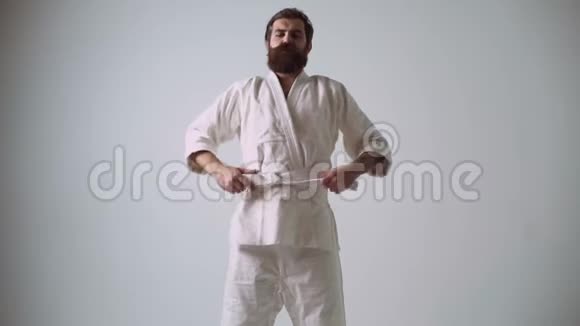 有趣的英俊男人用笨拙的动作与想象中的对手搏斗穿着白色的滑稽空手道战士视频的预览图