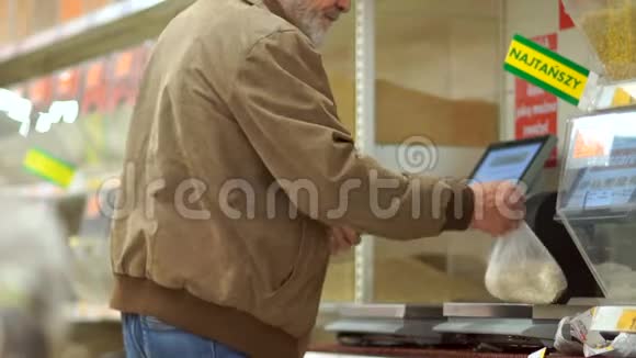 留着胡子的灰发退休人员在超市里用磅秤称麦片在包裹上贴上标价孤独的老视频的预览图
