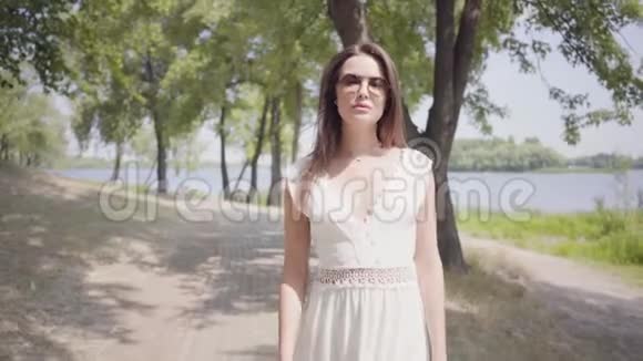 肖像迷人的年轻女孩黑发戴着太阳镜穿着长长的白色夏季时尚连衣裙散步视频的预览图