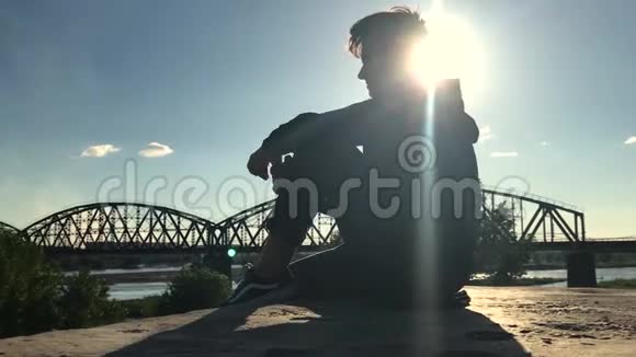亚洲少年坐在街边的桥的背景下视频的预览图