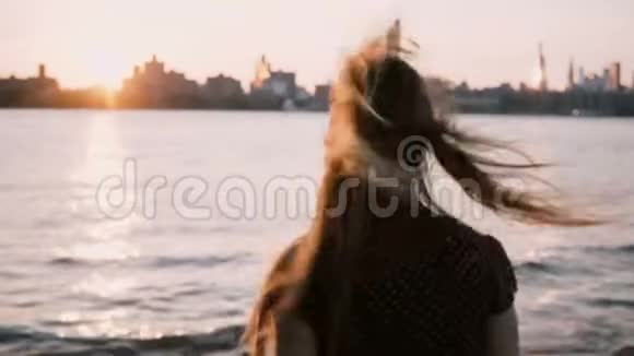 镜头跟随一个头发随风飘向水边的女孩停下来看纽约夕阳天际线视频的预览图