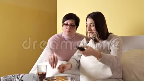 妈妈和女儿一边吃薯片一边喝电视一边喝可乐家里的舒适气氛视频的预览图
