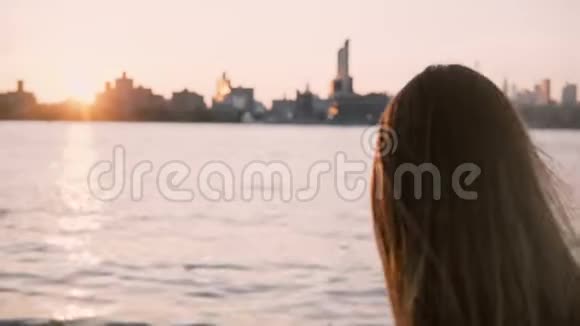 美丽的欧洲女孩长发在风中飘扬站在水边看着纽约的日落4K视频的预览图