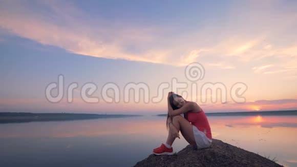 漂亮的年轻女子正平静地坐在湖边的石头上视频的预览图