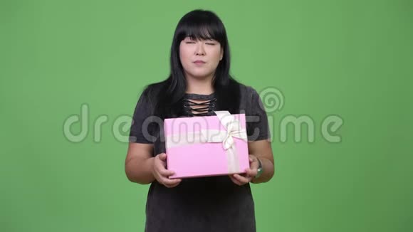 快乐超重的亚洲女人拿着礼品盒思考视频的预览图