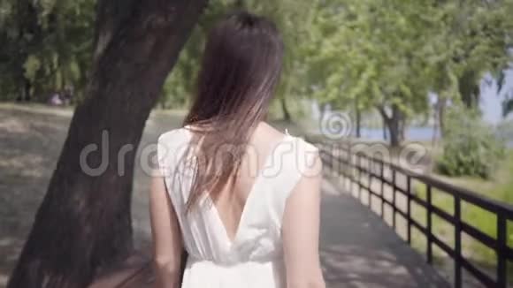 肖像可爱的年轻女孩一头黑发戴着太阳镜穿着白色的夏装走在路上视频的预览图