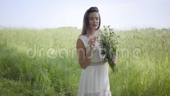 肖像可爱的年轻女孩黑发穿着一件白色的夏季时尚长裙站在田野上休闲视频的预览图